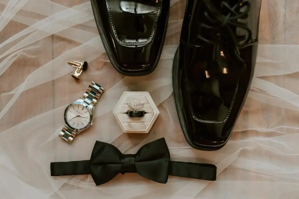 Flatlay of wedding invitations with green accents, bride’s shoes, jewelry, rings, and perfume styled for a Mississippi wedding.
